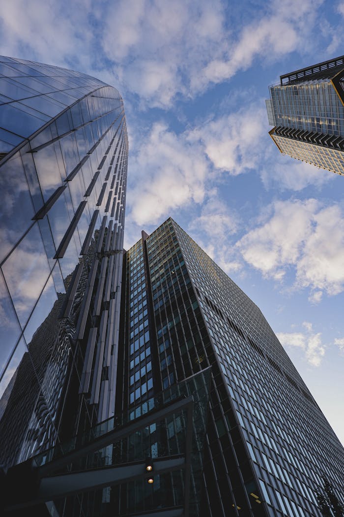 Low angle view of modern skyscrapers with a reflection on glass facades under a blue sky.